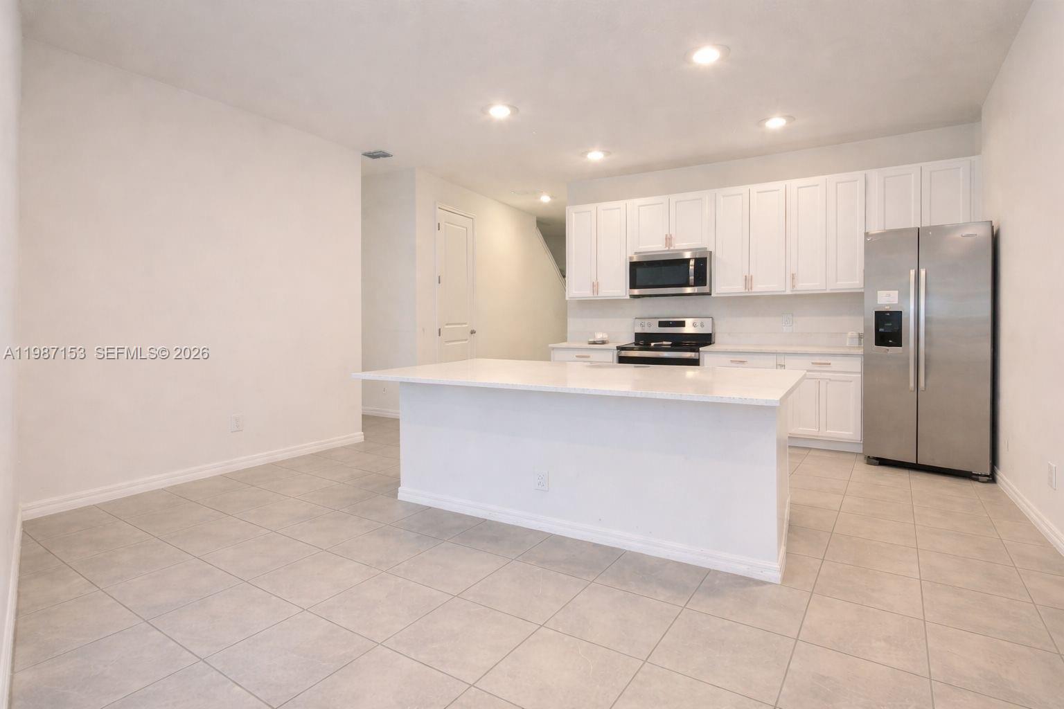A modern kitchen features white cabinets, stainless steel appliances, and a central island with seating — 1613 PELICAN DRIVE, Davenport FL 33896, DAVENPORT, FL