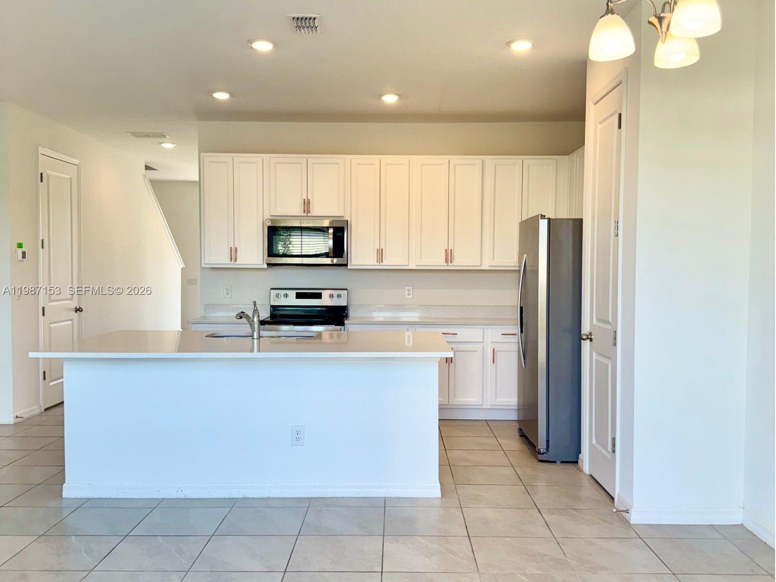 A kitchen features white cabinets, stainless steel appliances, a center island, and light tile flooring — 1613 PELICAN DRIVE, Davenport FL 33896, DAVENPORT, FL