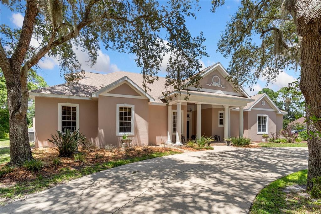 A single-story house with a beige stucco exterior, a columned porch, and a concrete driveway — 180 RIVER OAKS CIRCLE, SANFORD, FL