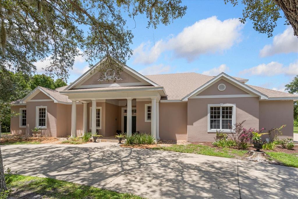 A single-story tan house with a columned front porch and a large concrete driveway — 180 RIVER OAKS CIRCLE, SANFORD, FL