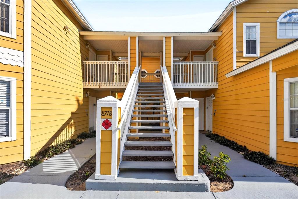 An exterior view of a yellow apartment building with a central staircase leading to balconies — 8718 RAIN FOREST PLACE UNIT C, KISSIMMEE, FL