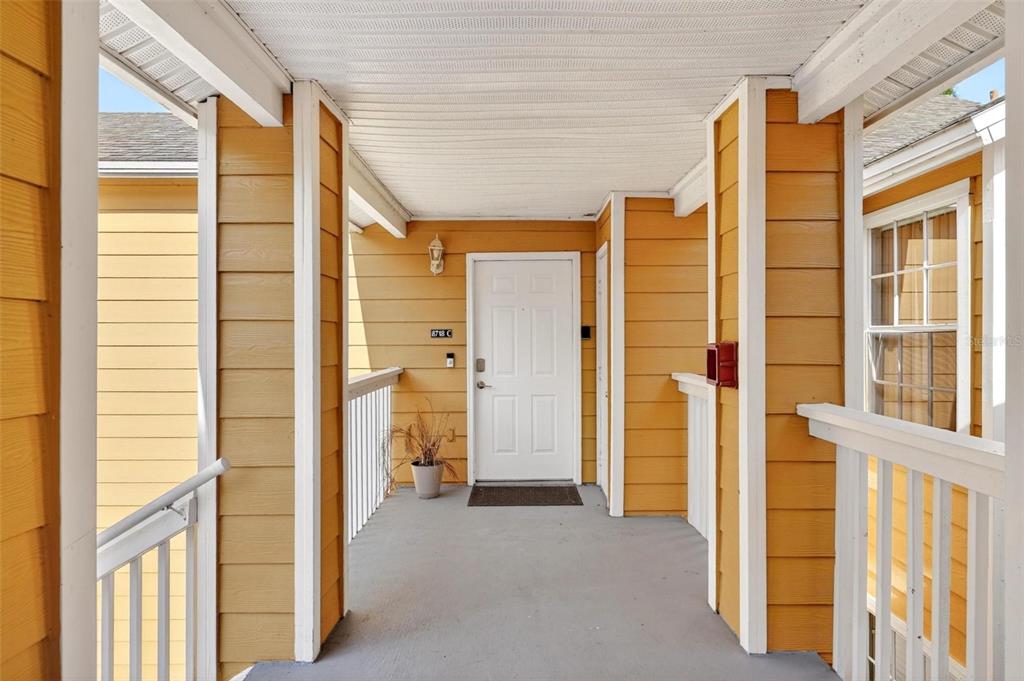 An exterior view of a covered apartment entryway with yellow siding and a white door — 8718 RAIN FOREST PLACE UNIT C, KISSIMMEE, FL