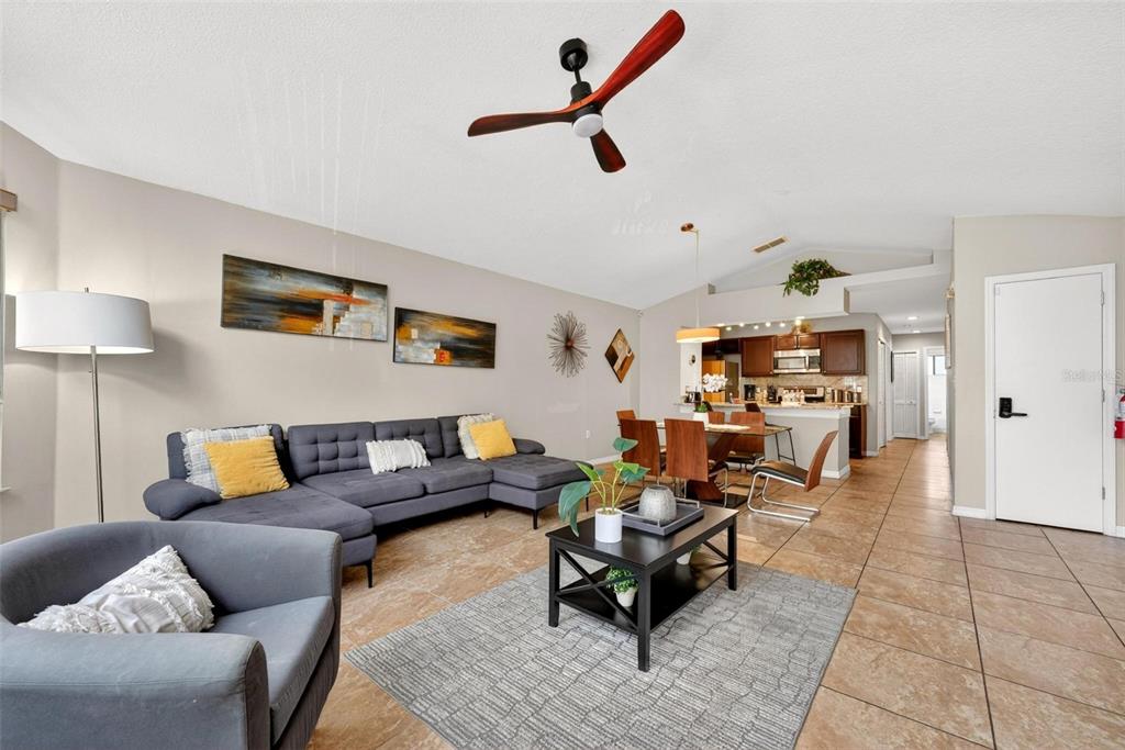 A living room with a gray sectional sofa, coffee table, and an open kitchen area — 8718 RAIN FOREST PLACE UNIT C, KISSIMMEE, FL
