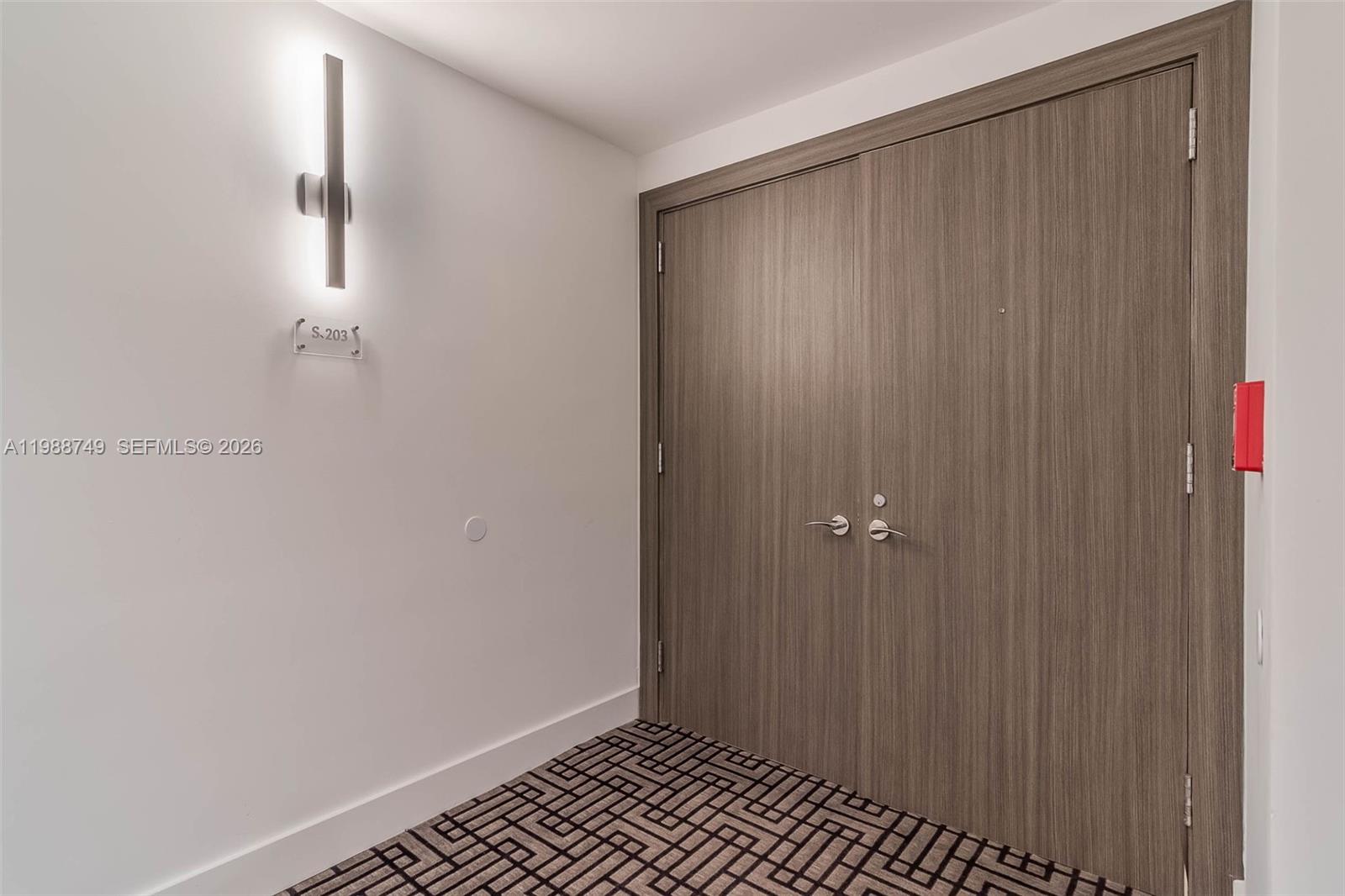 A hallway features a double door with wood-grain finish, patterned carpet, and a wall sconce — 3737 Collins Ave # 203, Miami Beach FL 33140, MIAMI BEACH, FL