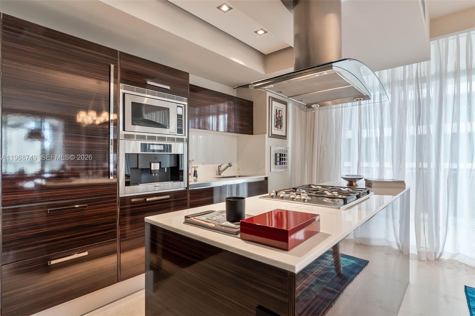 A modern kitchen features dark wood cabinetry, a white island countertop, and stainless steel appliances — 3737 Collins Ave # 203, Miami Beach FL 33140, MIAMI BEACH, FL