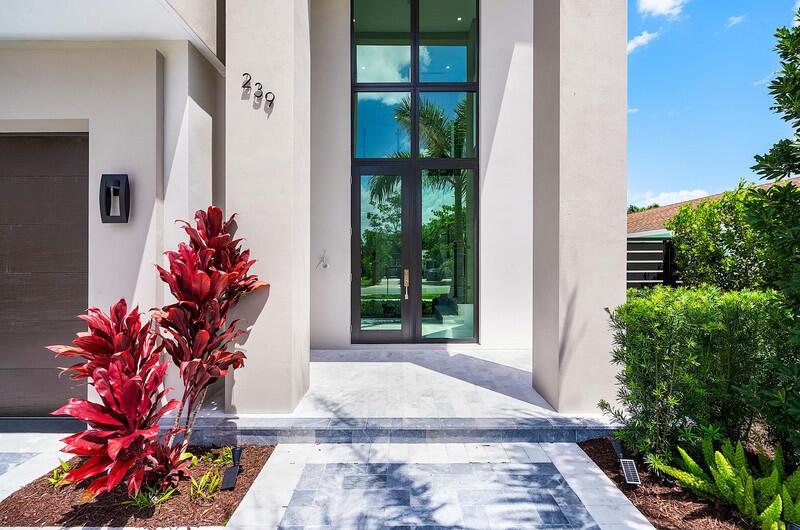 A modern home entrance features a glass front door, tall columns, and red foliage — 239 NE 11th Street, Delray Beach FL 33444, DELRAY BEACH, FL