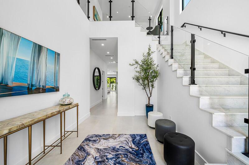 A bright foyer features a marble staircase, a console table, and a blue patterned rug — 239 NE 11th Street, Delray Beach FL 33444, DELRAY BEACH, FL