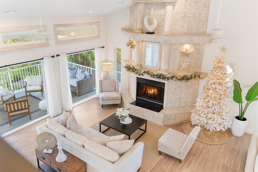 A living room with a stone fireplace, wood floors, and sliding doors overlooking the water — 255 46TH AVENUE, ST PETE BEACH, FL