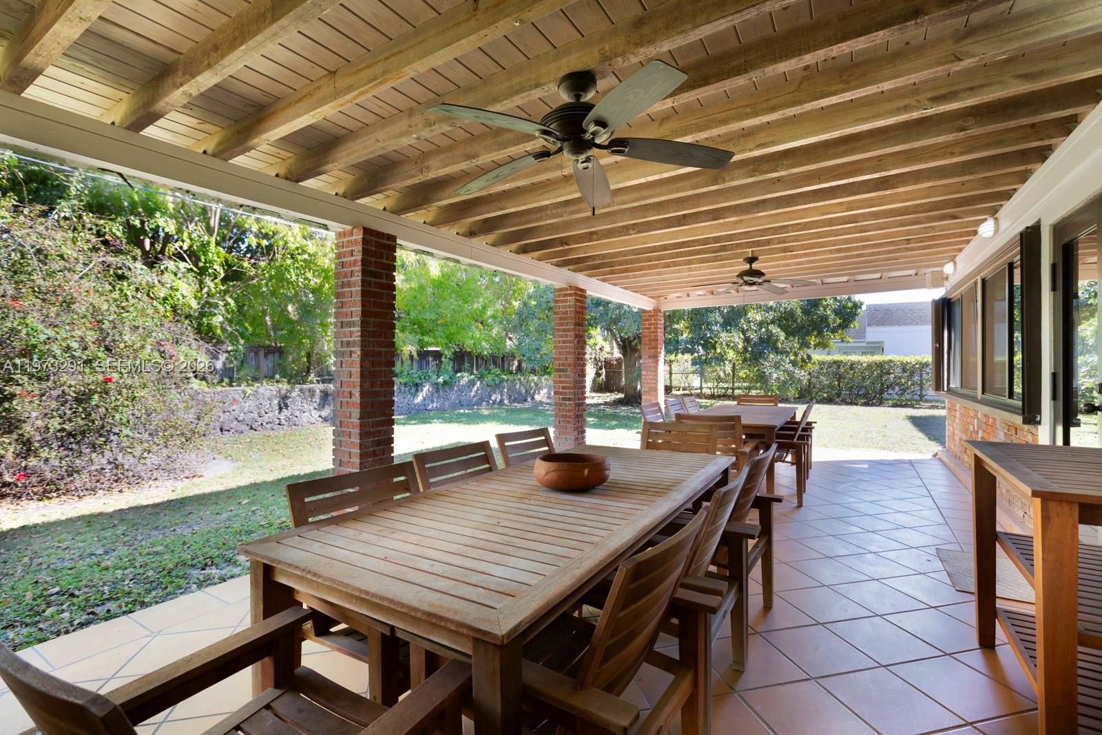 A covered outdoor patio features brick columns, wooden ceiling beams, ceiling fans, and dining furniture — 3721 SW 58th Ave, Miami FL 33155, MIAMI, FL