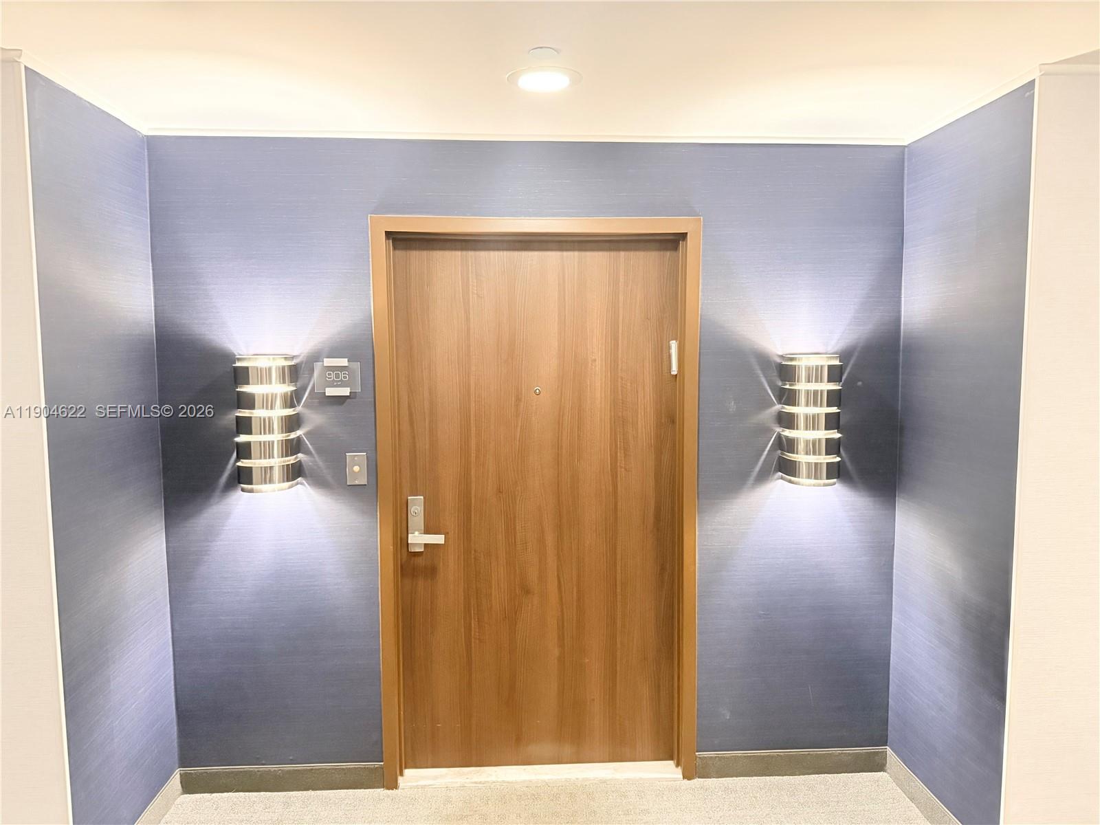A wooden door with a room number sign is flanked by two wall-mounted light fixtures — 10155 Collins Ave # 906, Bal Harbour FL 33154, BAL HARBOUR, FL