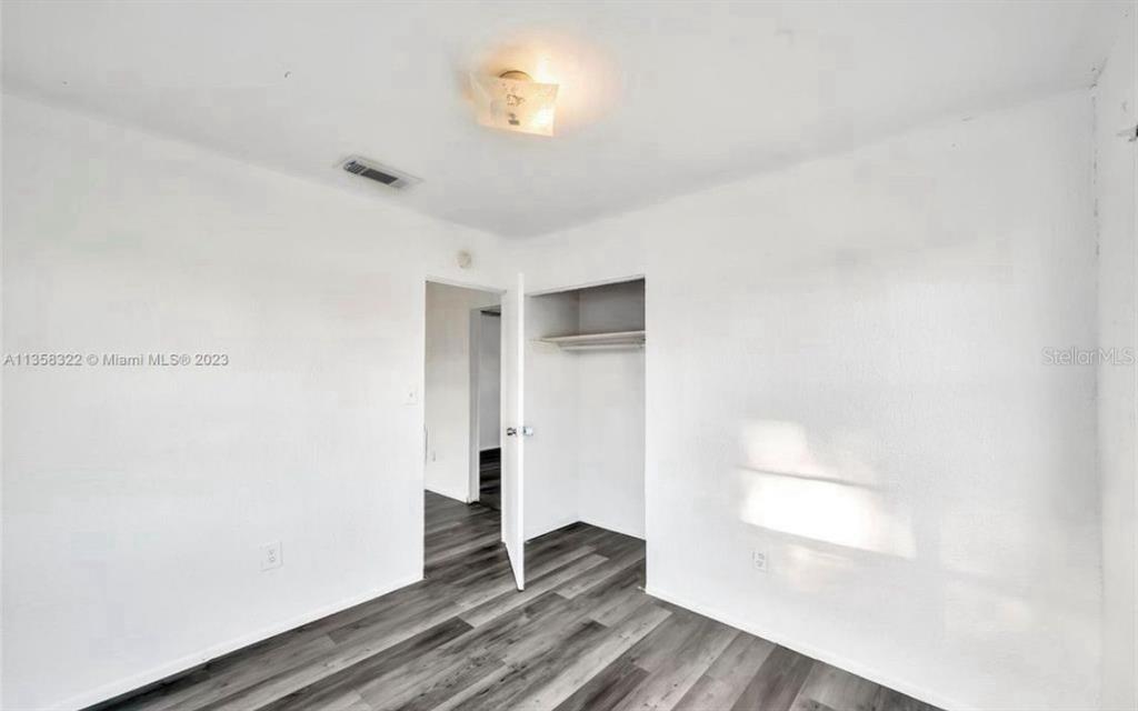 A bedroom features white walls, gray wood-look flooring, a ceiling light, and an open closet — 1001 N 16TH COURT, FORT PIERCE, FL