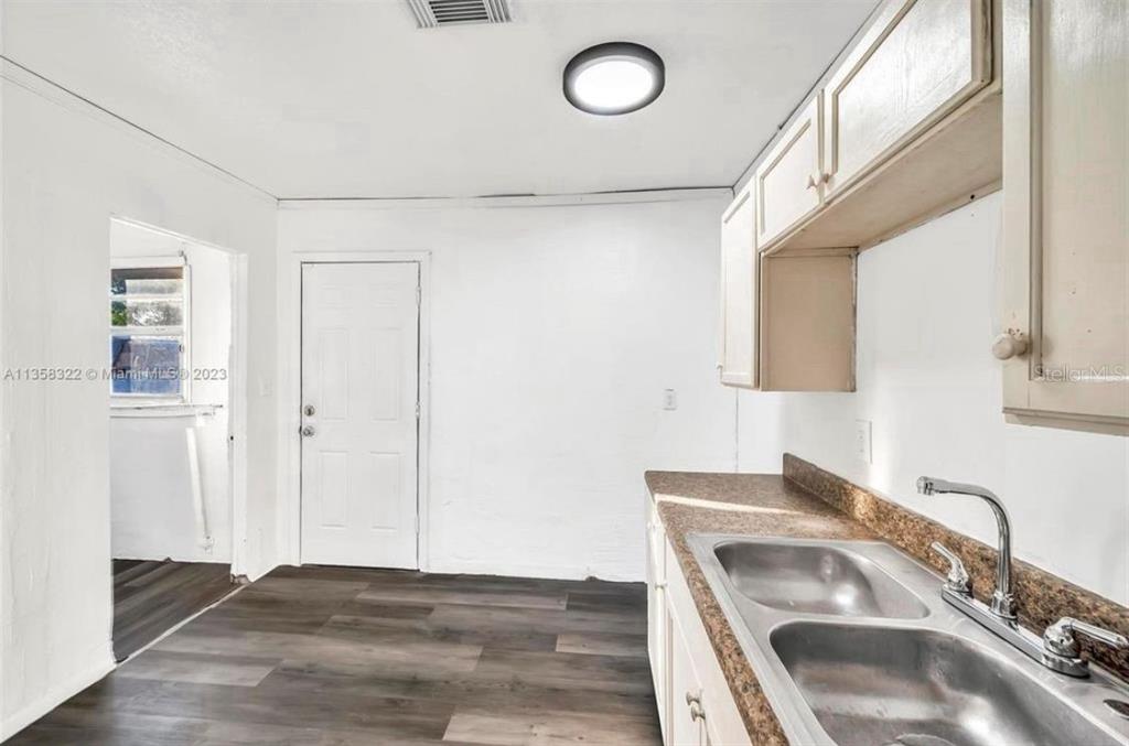 A kitchen features a double-basin stainless steel sink, wood-look flooring, and white cabinets — 1001 N 16TH COURT, FORT PIERCE, FL