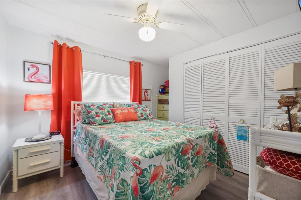A bedroom features a flamingo-patterned bedspread, orange curtains, white louvered closet doors, and a ceiling fan — 2100 KINGS HIGHWAY UNIT 59, PORT CHARLOTTE, FL