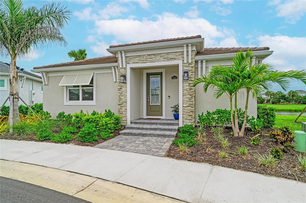 A single-story house features a stone-accented entryway, a paved walkway, and surrounding palm trees — 4064 SANTA CATERINA BOULEVARD UNIT 101, LAKEWOOD RANCH, FL