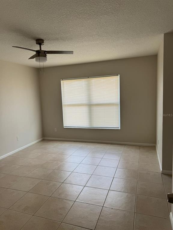 A bedroom with beige walls, a ceiling fan, and light-colored square floor tiles — 5272 LONESOME DOVE DRIVE, KISSIMMEE, FL