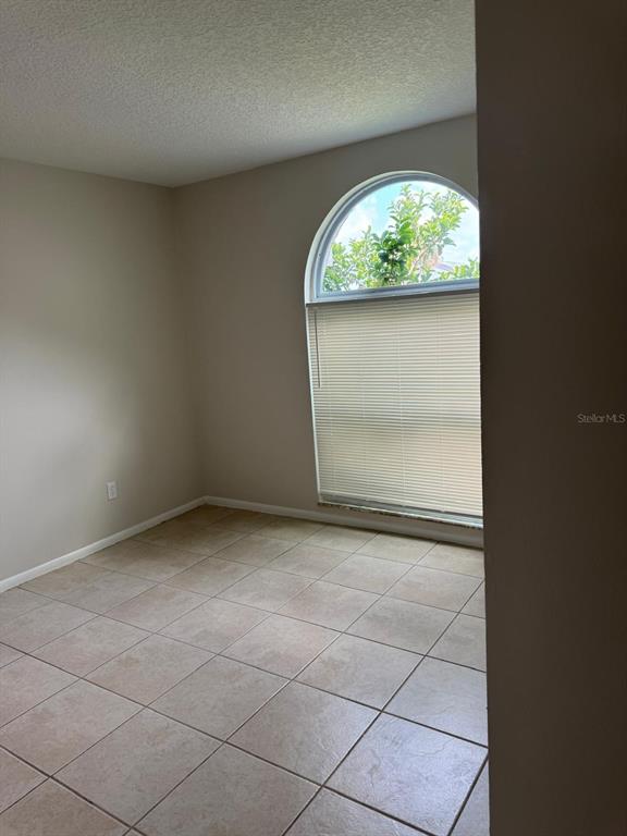 An empty room with beige tile flooring and a large arched window with blinds — 5272 LONESOME DOVE DRIVE, KISSIMMEE, FL