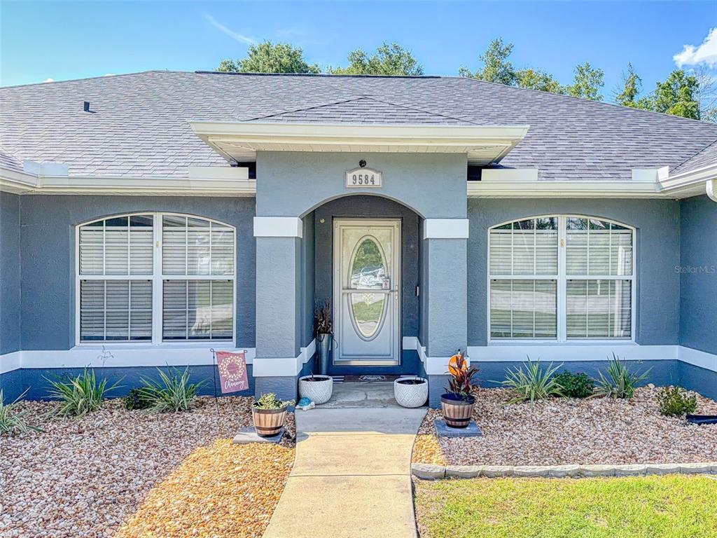 The exterior of a gray single-story house features a covered entryway and a stone walkway — 9584 SW 42ND COURT, OCALA, FL