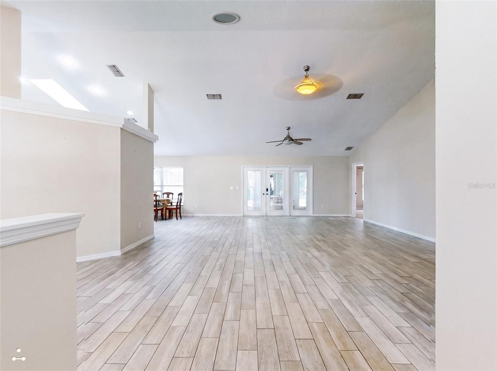 A spacious living area features light wood-look tile flooring, vaulted ceilings, and glass patio doors — 9584 SW 42ND COURT, OCALA, FL