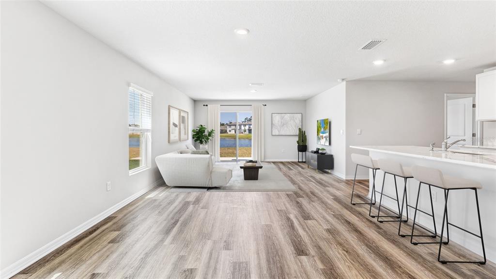 This open-concept living room features wood-look flooring, a kitchen island with bar stools, and sliding doors — 10632 HIDDEN BANKS GLEN, PARRISH, FL