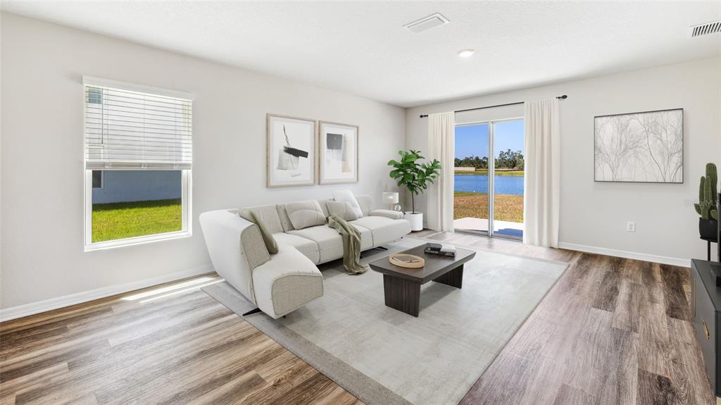 A living room features a sectional sofa, coffee table, wood-look flooring, and sliding glass doors — 10632 HIDDEN BANKS GLEN, PARRISH, FL