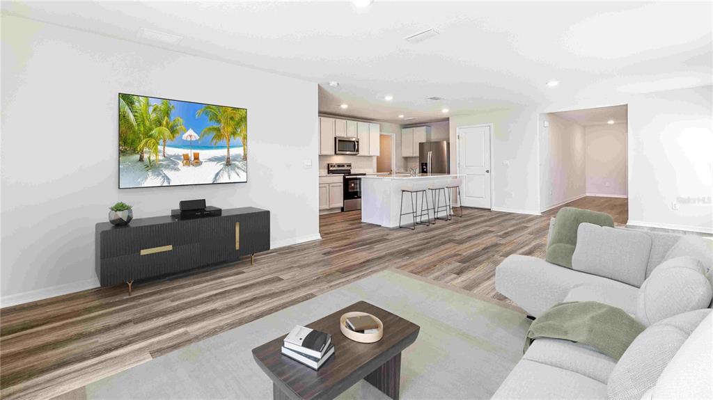 A living room with wood-look flooring, a wall-mounted television, and an open kitchen beyond — 10632 HIDDEN BANKS GLEN, PARRISH, FL