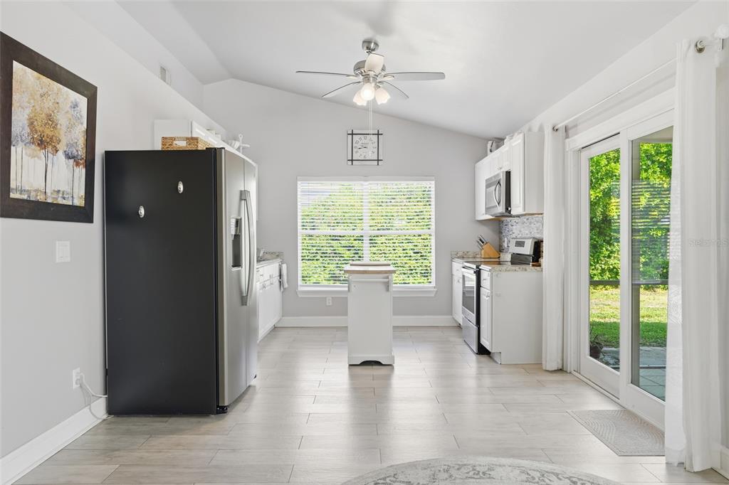 A bright kitchen features white cabinetry, stainless steel appliances, a center island, and tile flooring — 4934 SW 20TH PLACE, CAPE CORAL, FL