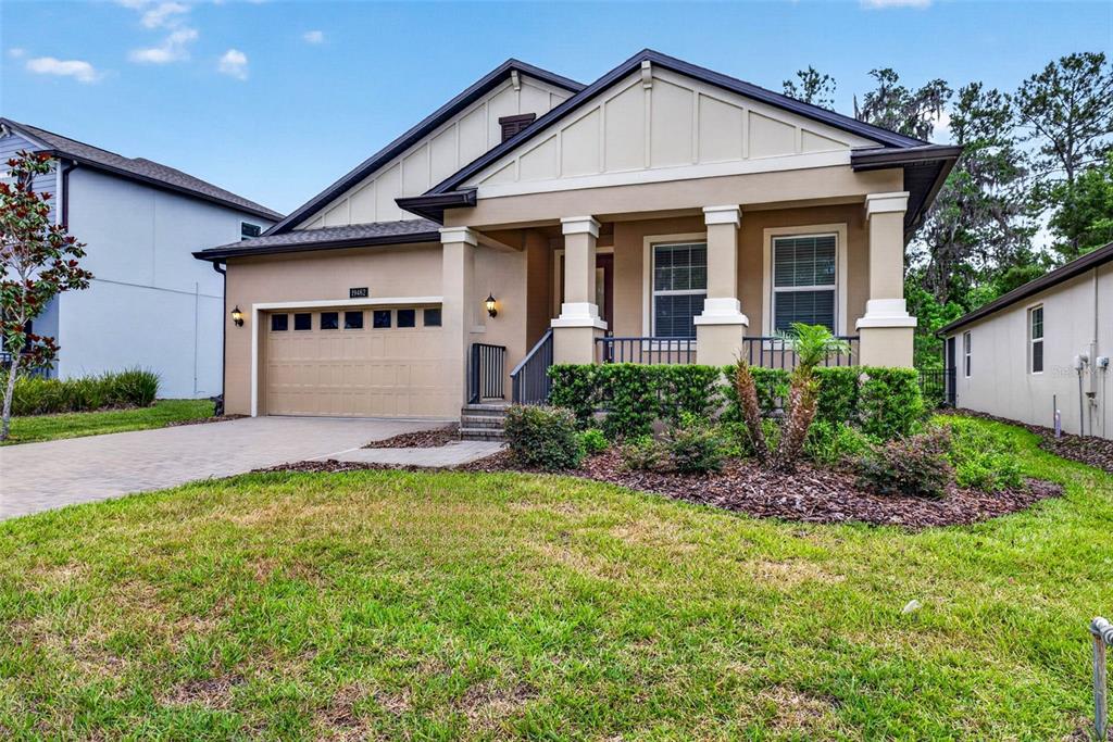 A tan single-story house with a two-car garage, front porch, and landscaped yard — 19462 FOREST GARDEN COURT, BROOKSVILLE, FL