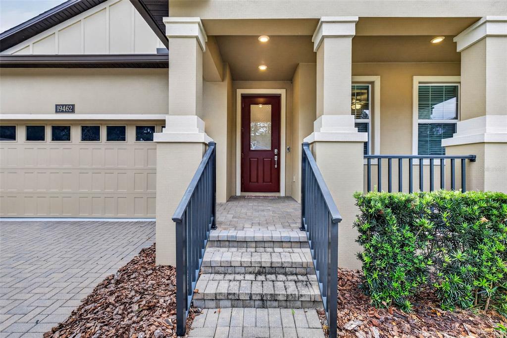 A paved walkway leads to the front entrance of a house with a red door — 19462 FOREST GARDEN COURT, BROOKSVILLE, FL