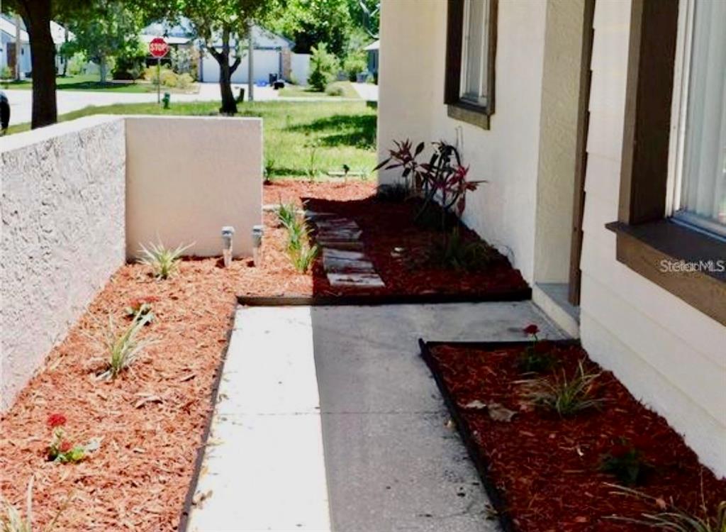 A concrete walkway leads to a house entrance flanked by mulch beds and small plants — 107 SHADY OAK DRIVE, SANFORD, FL