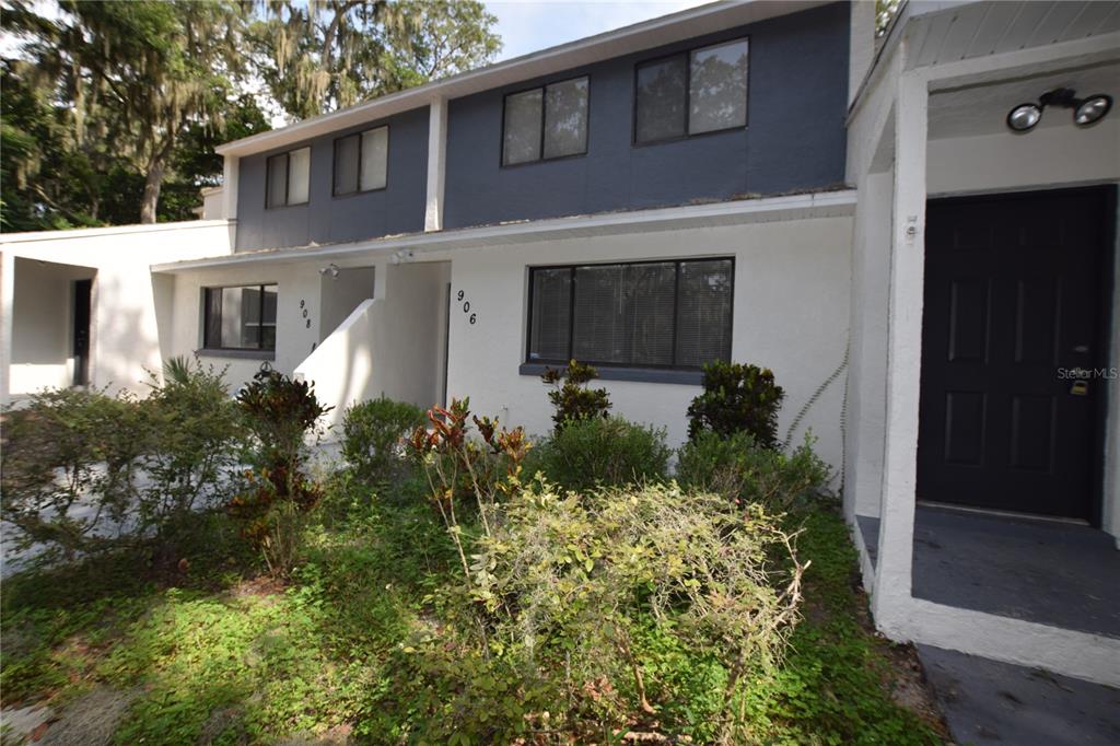 A two-story townhouse exterior with white stucco, dark blue siding, and a small front garden — 906 SUMTER STREET, LEESBURG, FL