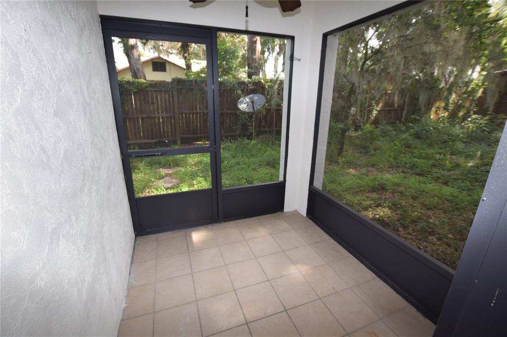 A tiled screened-in porch overlooks a backyard with a wooden fence and trees — 906 SUMTER STREET, LEESBURG, FL