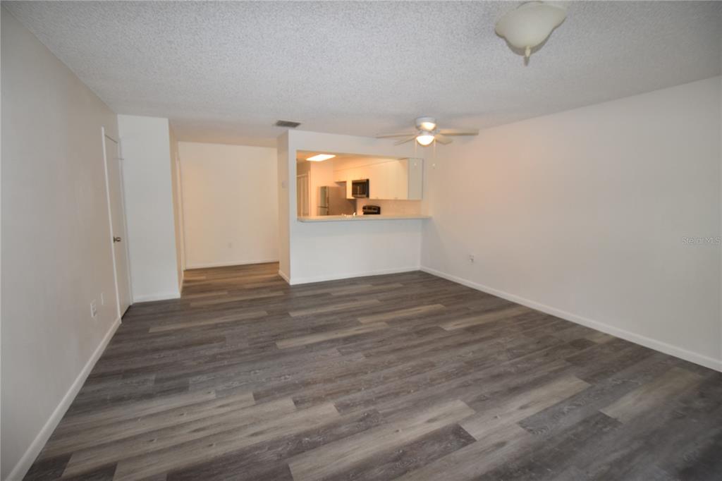 A living room with gray wood-look flooring, a ceiling fan, and a kitchen pass-through window — 906 SUMTER STREET, LEESBURG, FL