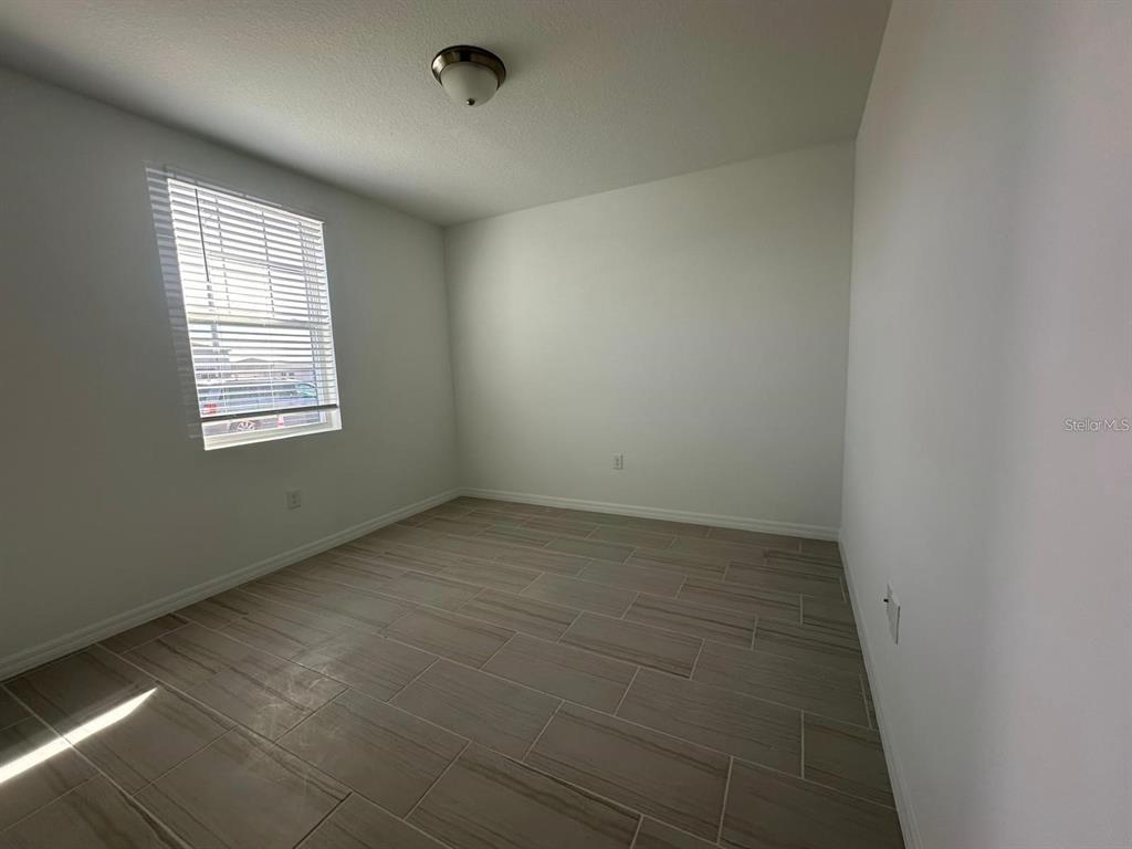 An empty room features white walls, a window with blinds, and light-colored tile flooring — 2748 SAN MARCO WAY, WINTER HAVEN, FL