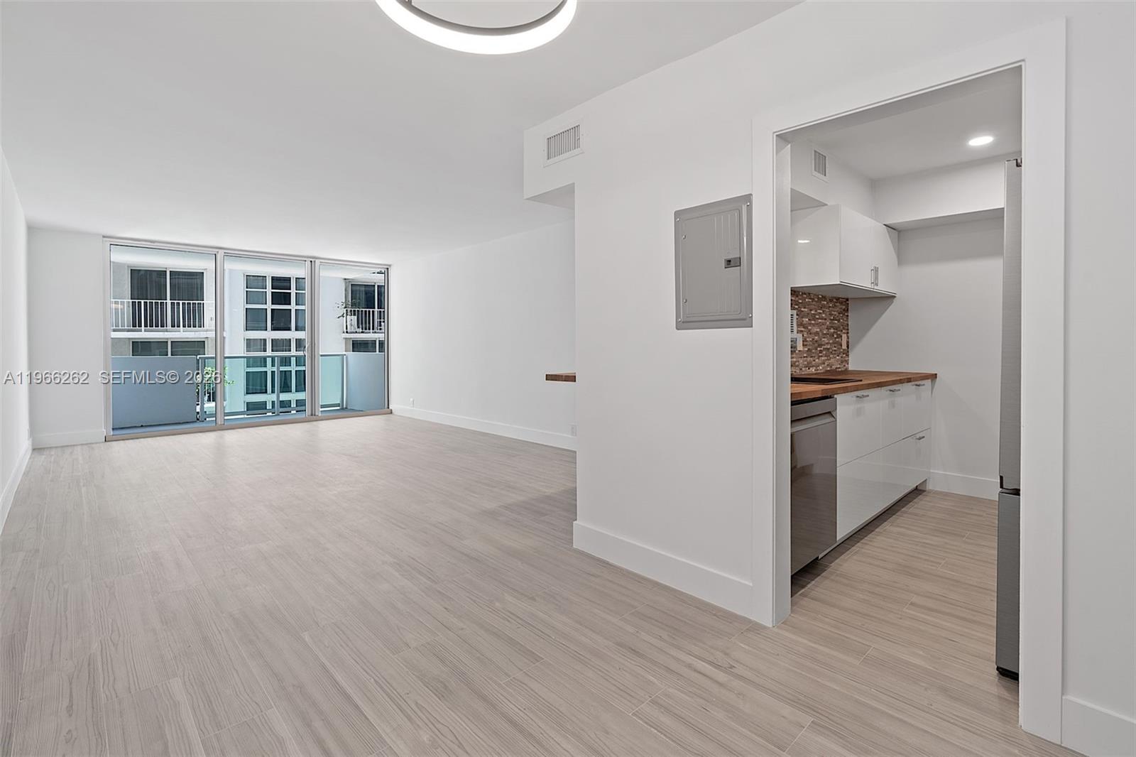 A bright living area with light wood-look flooring leads to a compact kitchen with white cabinets — 1200 West Ave # 521, Miami Beach FL 33139, MIAMI BEACH, FL