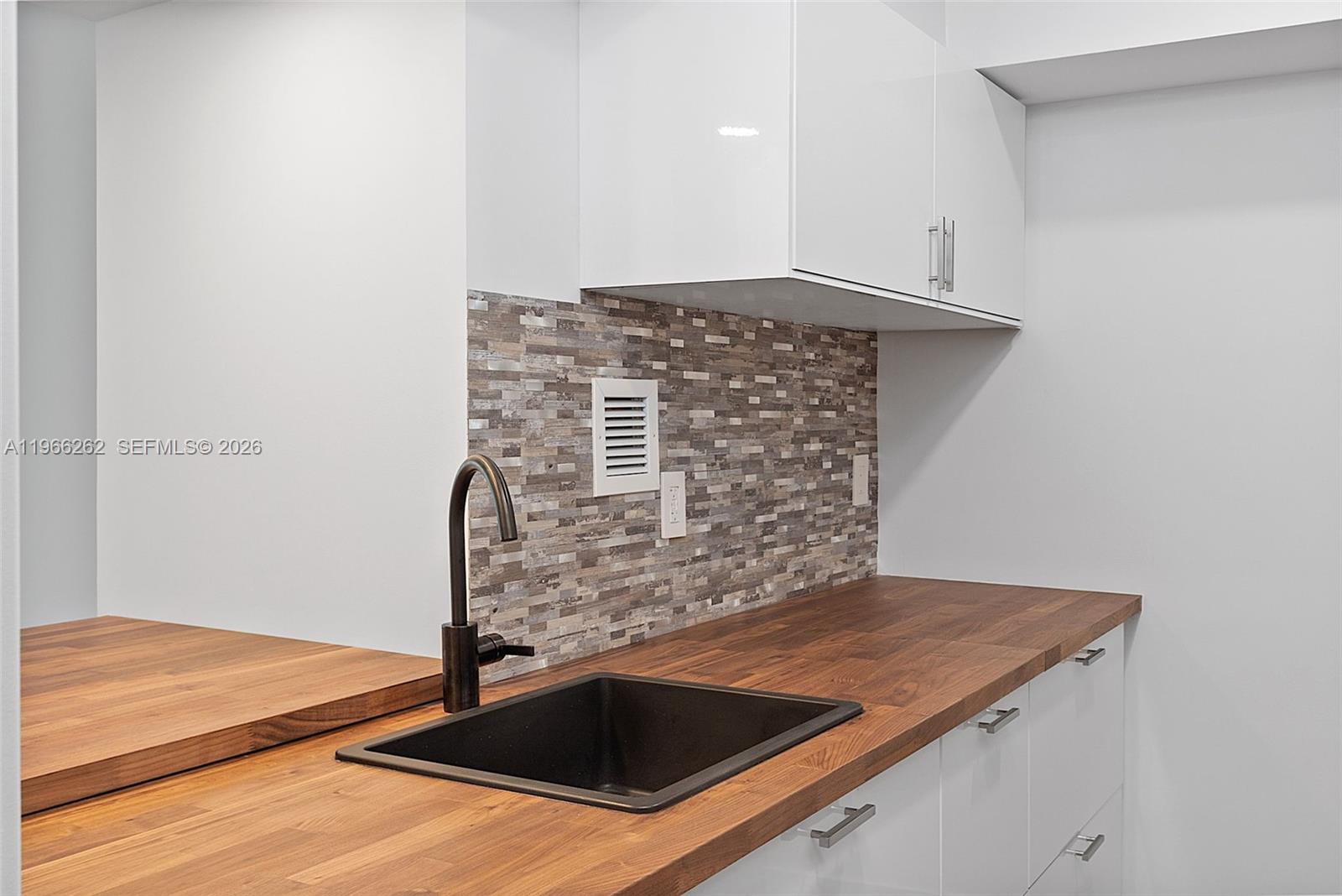 A kitchen features a dark sink, wood countertop, white cabinets, and a mosaic tile backsplash — 1200 West Ave # 521, Miami Beach FL 33139, MIAMI BEACH, FL