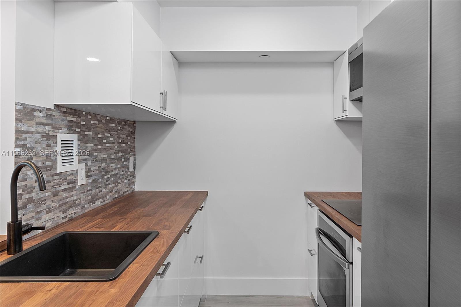 A galley kitchen features white cabinets, wood countertops, a black sink, and a tiled backsplash — 1200 West Ave # 521, Miami Beach FL 33139, MIAMI BEACH, FL