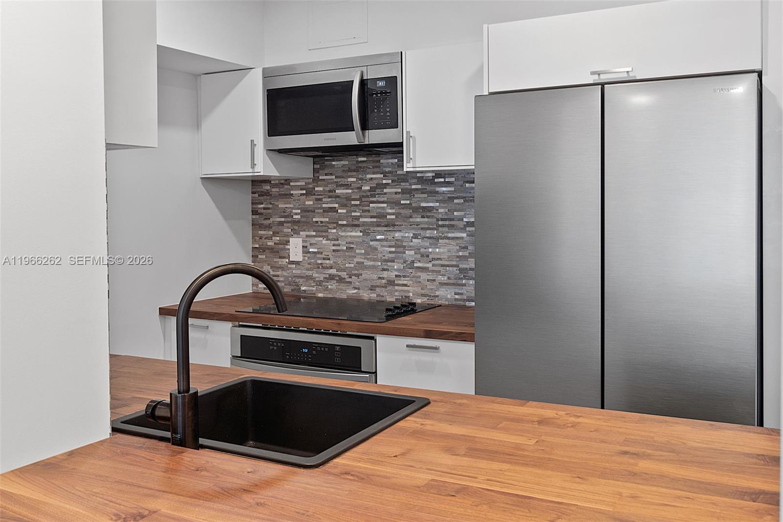 A kitchen features white cabinets, stainless steel appliances, a tiled backsplash, and wood countertops — 1200 West Ave # 521, Miami Beach FL 33139, MIAMI BEACH, FL