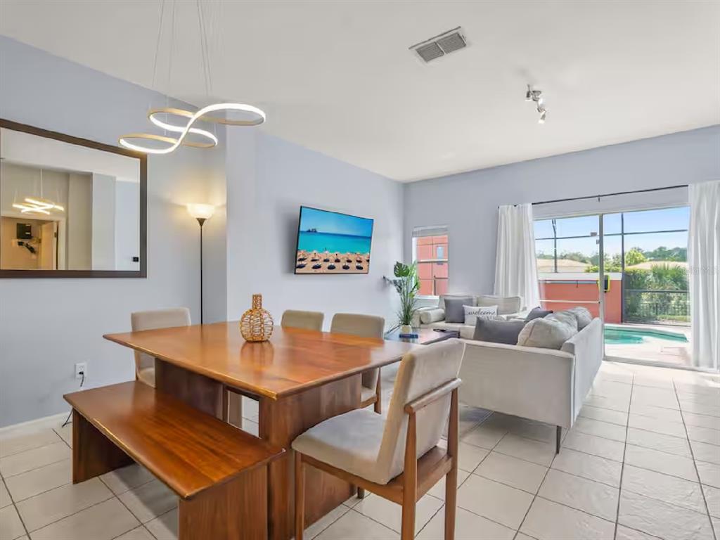 A dining area with a wooden table and bench opens into a living room with pool views — 3113 YELLOW LANTANA LANE, KISSIMMEE, FL