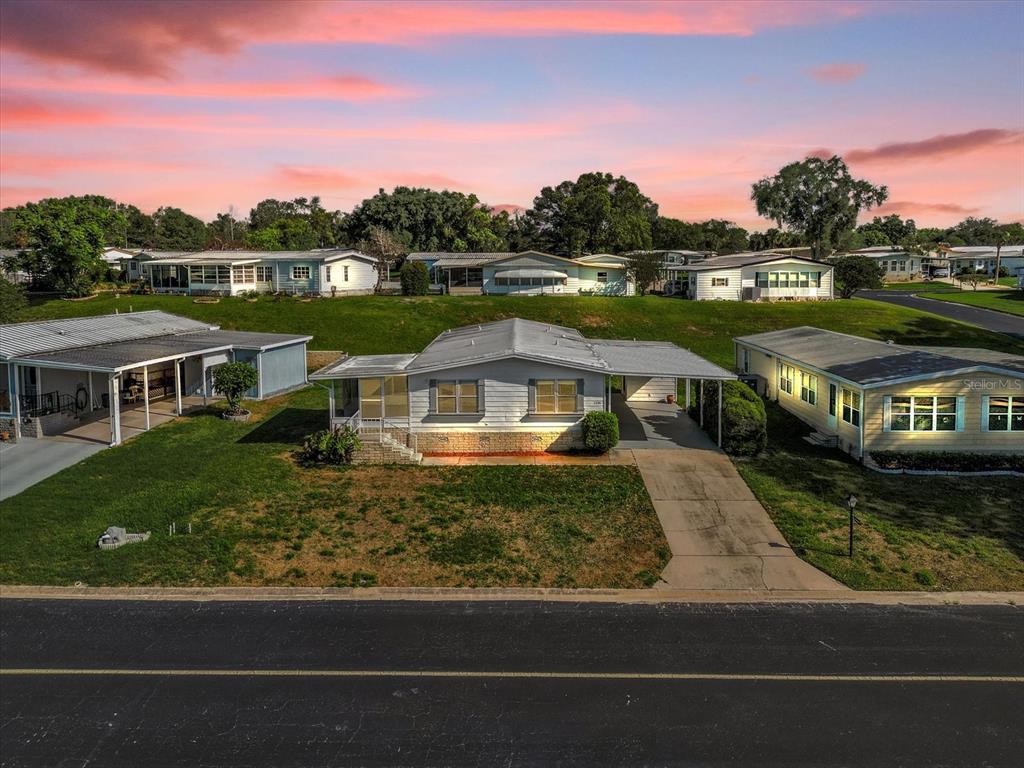 An exterior view of a single-story manufactured home with a carport and a grassy lawn — 3338 N CITRUS CIRCLE UNIT 1679, ZELLWOOD, FL