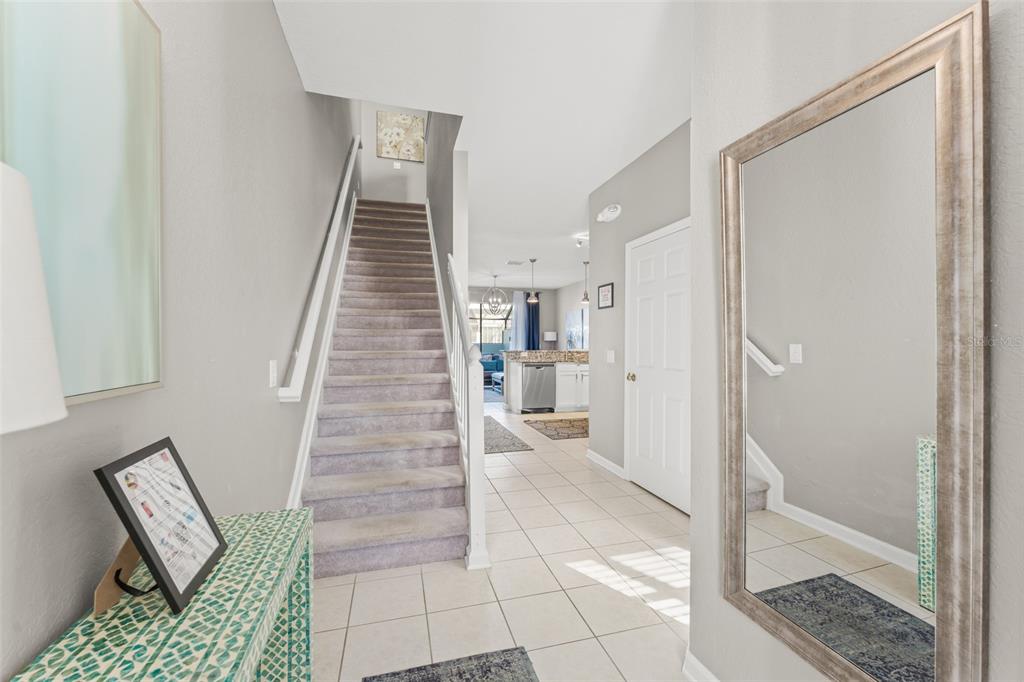 An entryway features a carpeted staircase, tiled flooring, a large wall mirror, and a console table — 7681 SIR KAUFMANN COURT, KISSIMMEE, FL