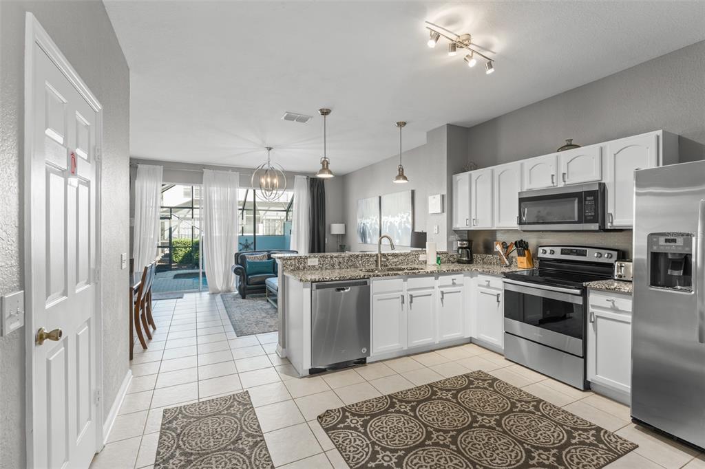 A kitchen with white cabinets and stainless steel appliances opens to a living area — 7681 SIR KAUFMANN COURT, KISSIMMEE, FL