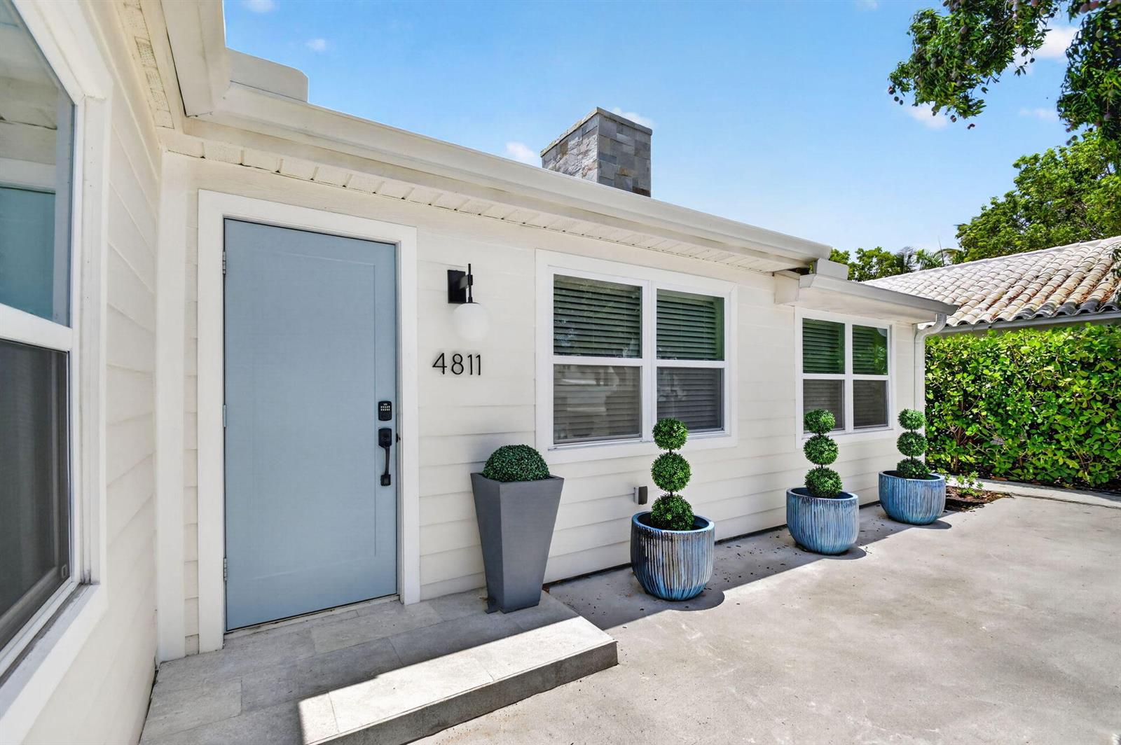 The exterior of a white house features a light blue door, three potted topiaries, and a chimney — 4811 N Flagler Drive, West Palm Beach FL 33407, WEST PALM BEACH, FL