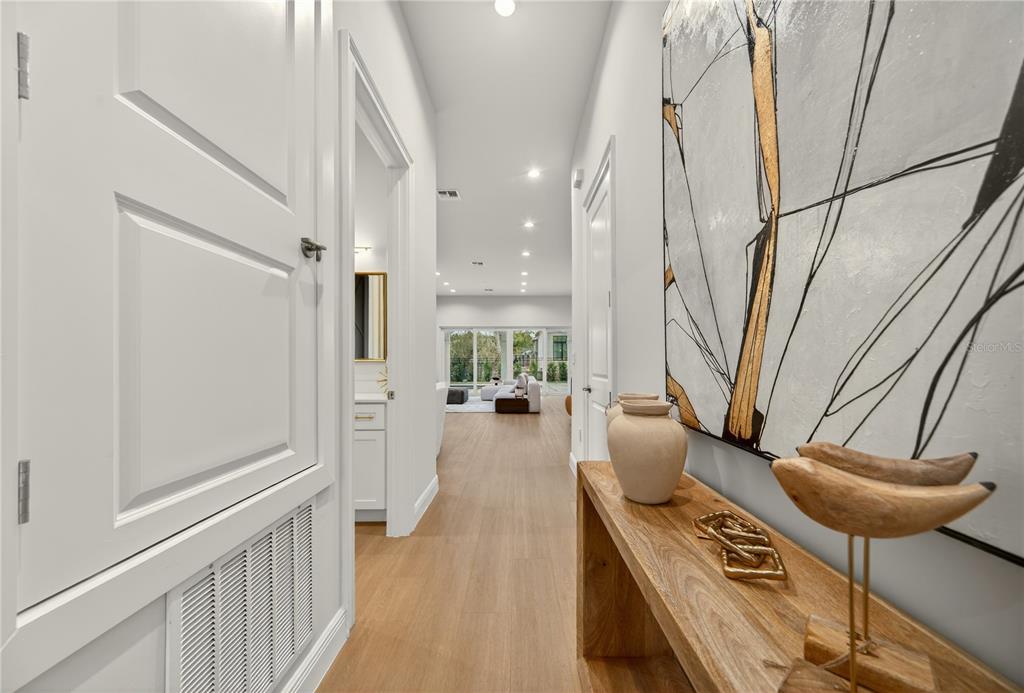 A hallway with light wood floors leads toward a bright living area with large windows — 1473 BERKSHIRE AVENUE, WINTER PARK, FL