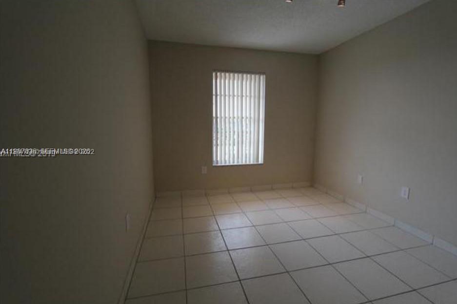 An empty room features beige walls, white tile flooring, and a window with vertical blinds — 5775 W 20th Ave # 406, Hialeah FL 33012, HIALEAH, FL
