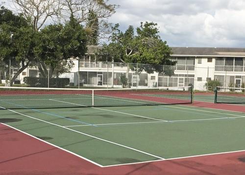 A tennis court with a net is situated in front of a multi-story residential building — 4509 3RD STREET CIRCLE W UNIT 283, BRADENTON, FL