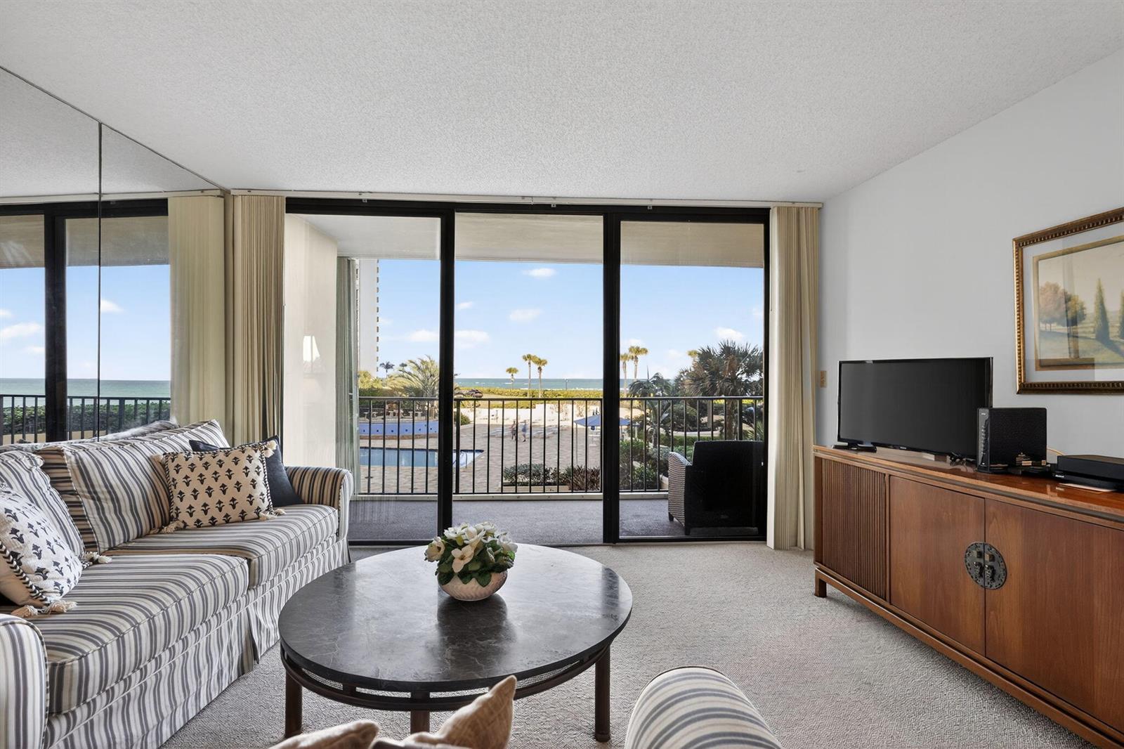 A living room with striped furniture, a round coffee table, and a balcony overlooking the ocean — 100 Ocean Trail Way # 204, Jupiter FL 33477, JUPITER, FL