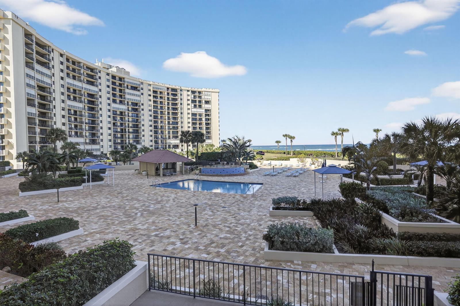 A large apartment building overlooks a paved pool deck with a swimming pool and landscaping — 100 Ocean Trail Way # 204, Jupiter FL 33477, JUPITER, FL