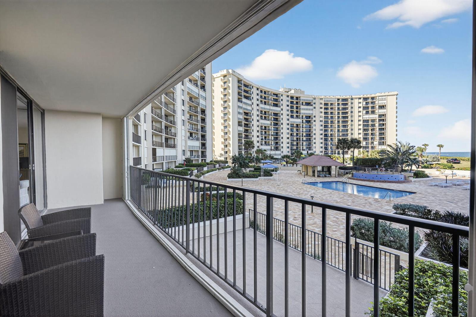 A balcony with wicker chairs overlooks a swimming pool and a large residential apartment complex — 100 Ocean Trail Way # 204, Jupiter FL 33477, JUPITER, FL