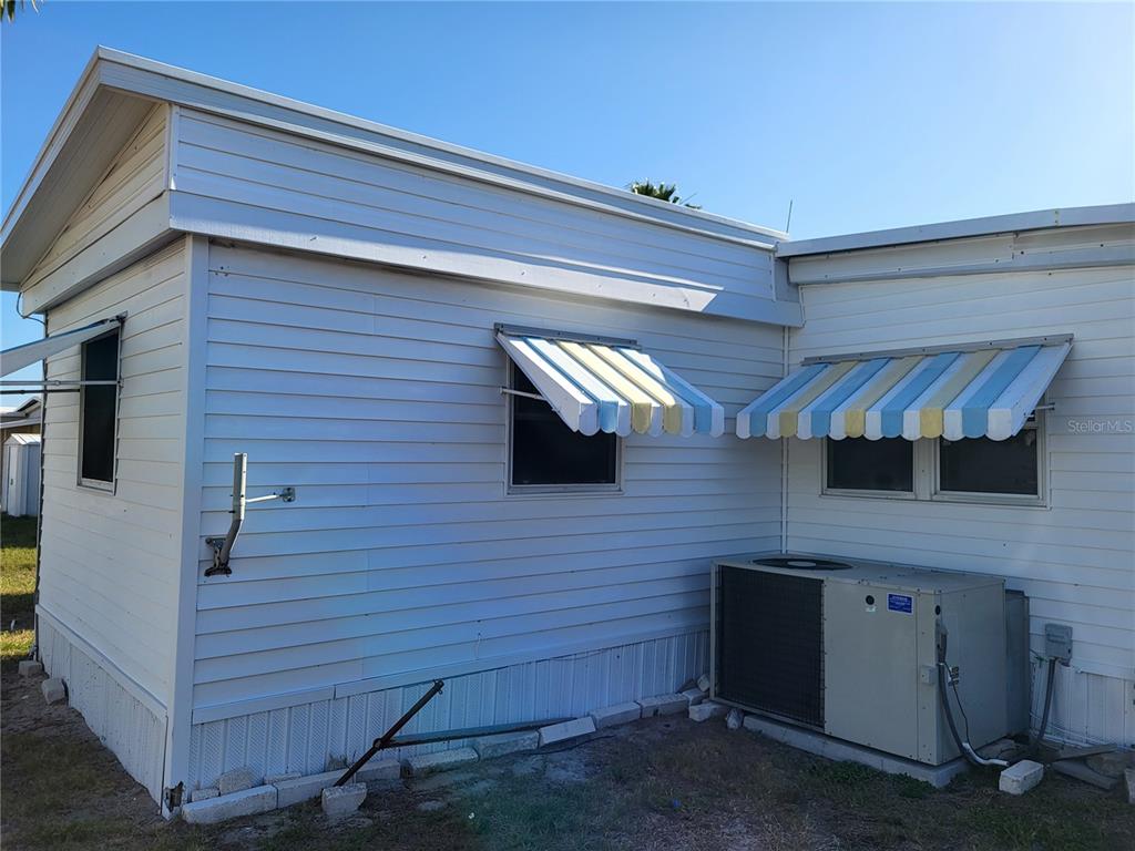 The exterior of a white mobile home features two striped awnings and an air conditioner — 12017 CARTWRIGHT DRIVE, HUDSON, FL