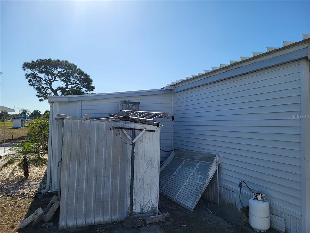 The exterior of a manufactured home features light-colored siding, a shed, and a propane tank — 12017 CARTWRIGHT DRIVE, HUDSON, FL